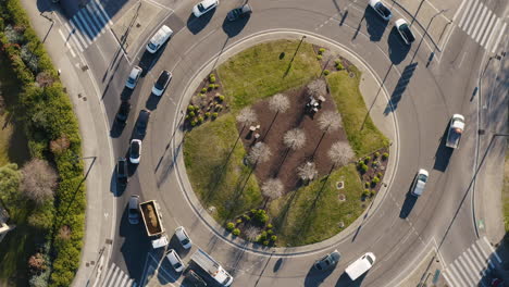 Circular-camera-drone-shot-over-a-green-roundabout-with-traffic-cars-sunset-time